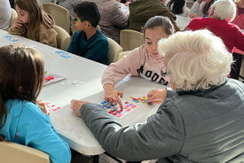 Photo où l'on voit des enfants assis à table avec une personne âgée lors d'un loto intergénérationnel organisé par l'accueil de loisirs