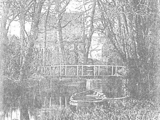 Photo très ancienne en noir et blanc. On voit un paysage extérieur avec des arbres et un pont