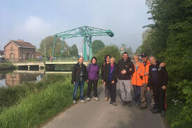 Sur cette photo, on voit un groupe de personnes posant sur un chemin bordant un cours d'eau. En arrière plan on distingue une grue bleue