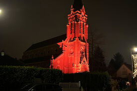 Photo de nuit avec le clocher de l'église illuminé en rouge.
