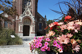 Photo de l'entrée de l'église. Au premier plan un parterre de fleurs.