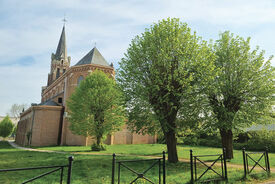 Vue arrière, en plan large, de l'église. Au premier plan on voit 3 arbres et de la verdure.