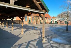 Photo de la cour de l'école primaire. A gauche d l'image on voit un préau en bois, à droite on voit la cour. Au fond on distingue les bâtiments de l'école.