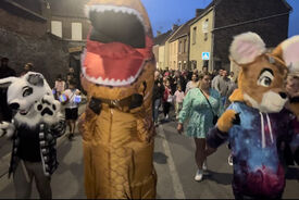 Photo prise dans la rue où on voit au premier plan 3 mascottes, une de renard blanc, une de renard marron et une de monstre, et en second plan des gens qui suivent.